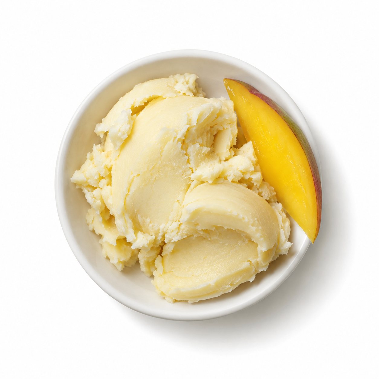 Overhead photograph of mango butter with a mango slice on white